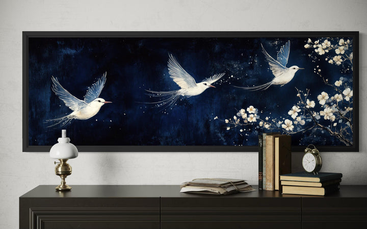 A long narrow canvas print of three white birds flying against a navy blue floral background.