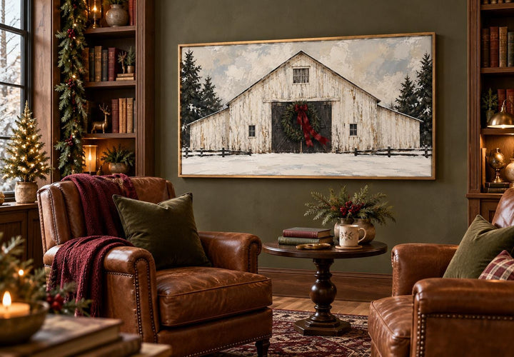 Framed canvas art of a white barn with an evergreen wreath and burgundy bow in a winter landscape.