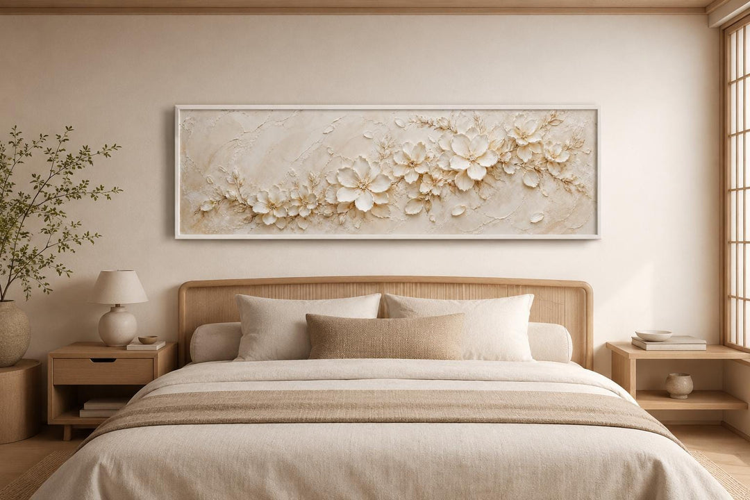 Long horizontal canvas with textured white floral art above a bed in a neutral-toned bedroom.