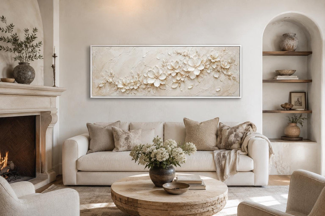 Long horizontal white floral canvas art above a sofa in a neutral, minimalist living room.