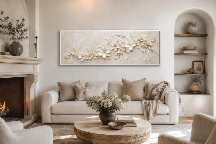 Long horizontal white floral canvas art above a sofa in a neutral, minimalist living room.