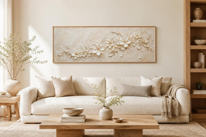 Long horizontal canvas with textured white floral art above a neutral sofa in a minimalist room.