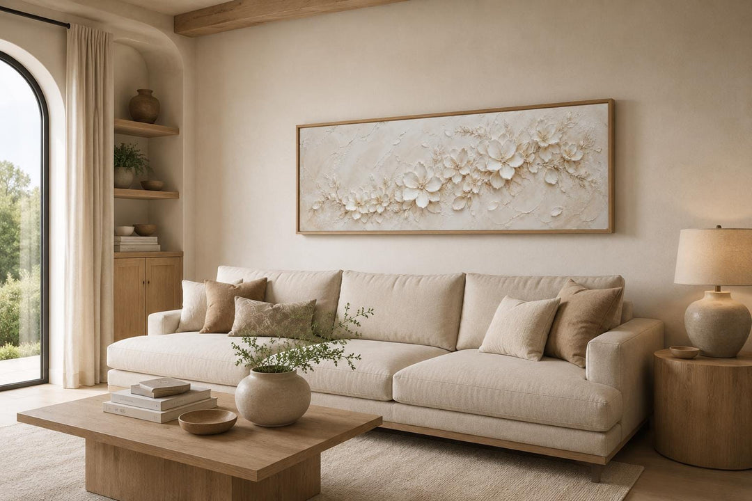 Long horizontal white floral canvas wall art with textured 3D-effect blossoms above a beige sofa.