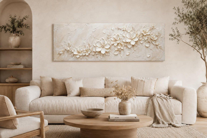 Long horizontal white floral canvas art with textured ivory blossoms above a neutral sofa.