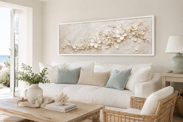 Long horizontal white floral canvas wall art with textured ivory blossoms above a white sofa.
