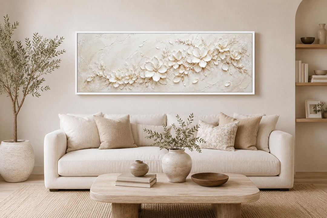 Long horizontal canvas with white textured floral art above a neutral sofa in a minimalist room.