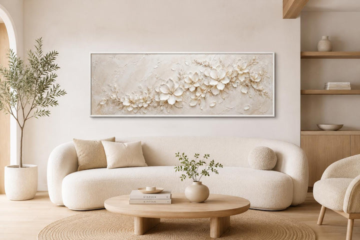 Long horizontal canvas with textured white floral art above a cream sofa in a neutral living room.