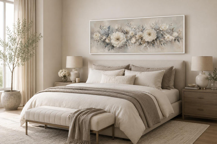 Long horizontal canvas print of white peonies in a neutral bedroom above a bed.