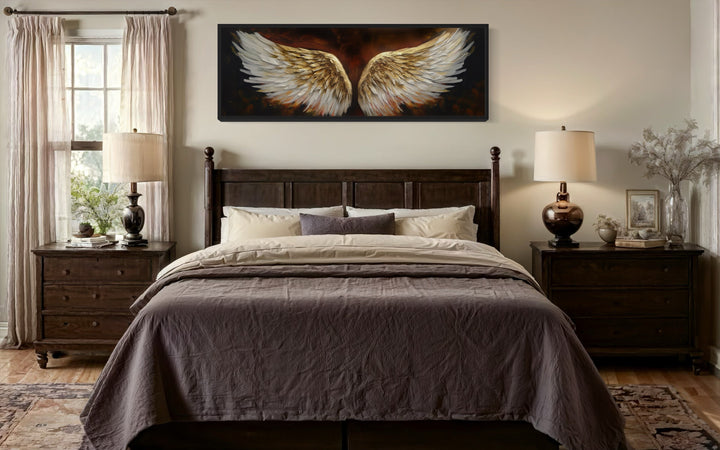 White gold angel wings on brown background horizontal framed canvas wall art above a bed.