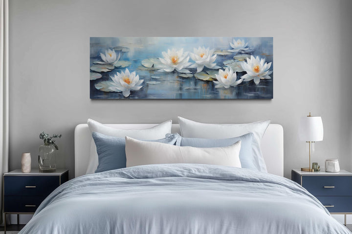 Horizontal canvas wall art of white lotus flowers on blue water displayed above a bed.
