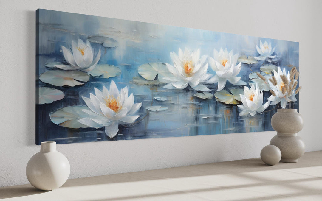 Horizontal canvas wall art of white lotus flowers floating on a blue pond above a neutral surface.