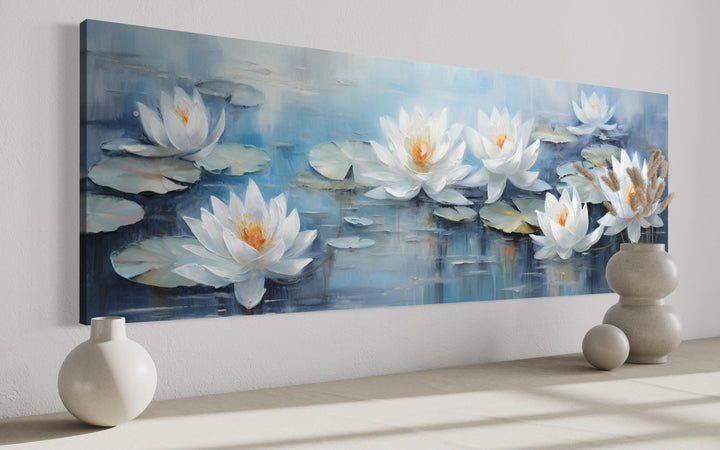 Horizontal canvas wall art of white lotus flowers floating on a blue pond above a neutral surface.