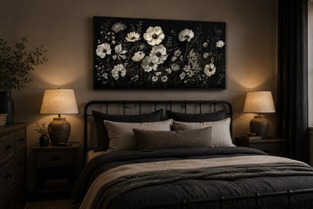 Framed canvas wall art of white wildflowers on a black background above a bed in a moody bedroom.