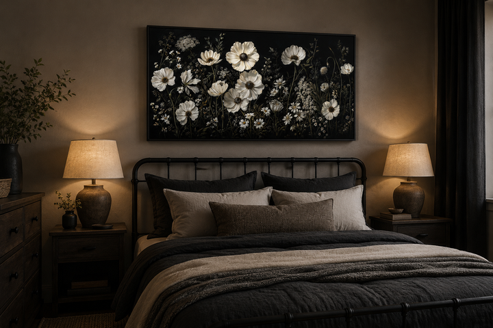 Framed canvas wall art of white wildflowers on a black background above a bed in a moody bedroom.