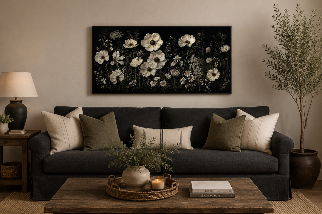 White wildflowers on black background moody framed canvas wall art above a dark sofa.