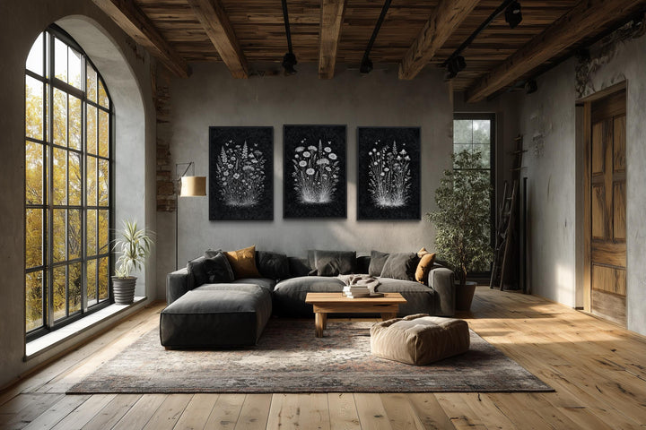 Set of three rustic canvas prints featuring white wildflowers on a black background in a living room.