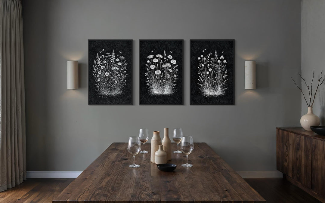 Set of three black and white wildflower canvas prints displayed in a moody, rustic dining room.