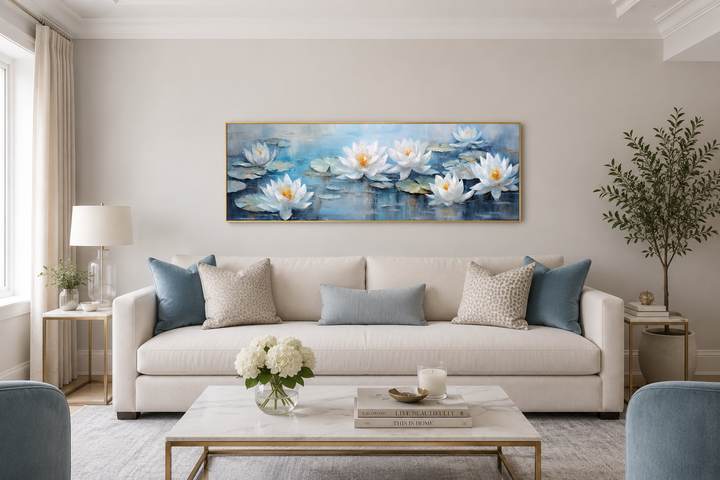 Horizontal canvas wall art of white lotus flowers on a blue pond above a cream sofa.