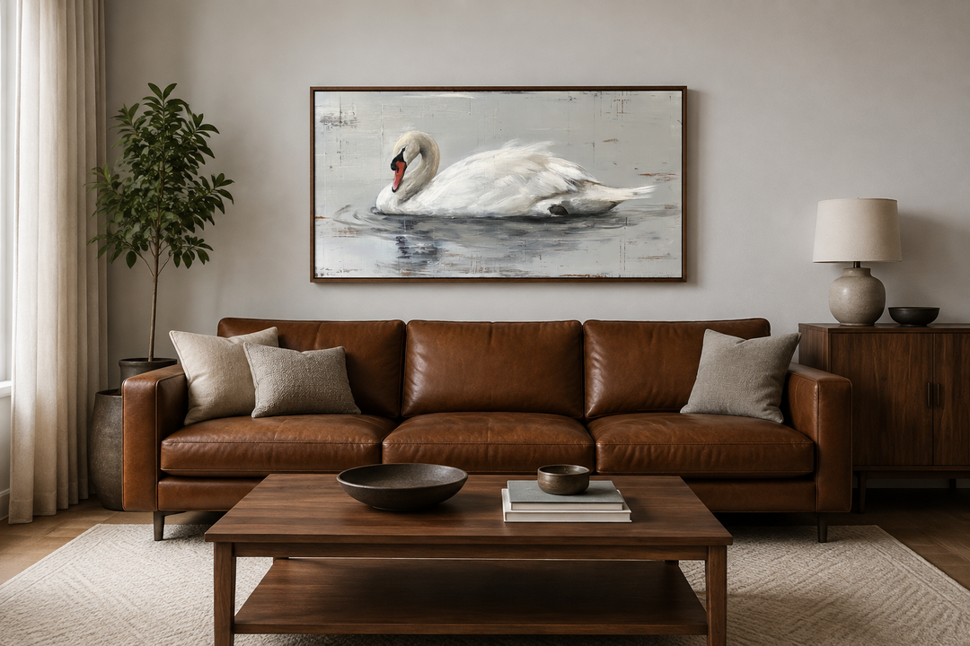 Framed white swan canvas painting hanging above a brown leather sofa in a rustic living room.
