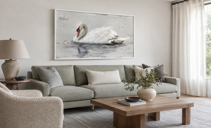 White swan rustic canvas painting in a white frame hanging above a green sofa in a living room.