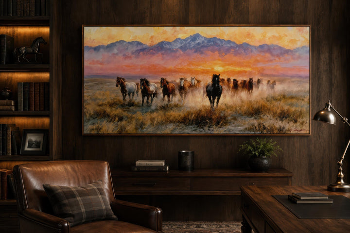 A wide canvas print of wild mustangs running across a plain under a vibrant sunset in a rustic room.