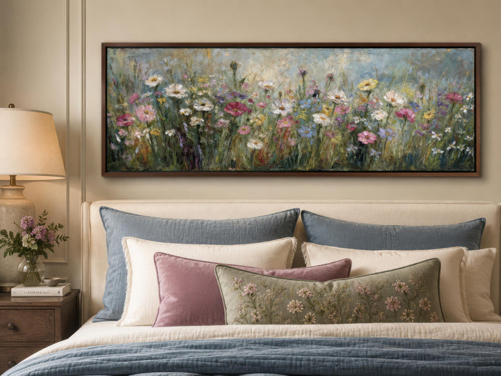 A long narrow canvas painting of a colorful wildflower field hangs above a bed with layered pillows.