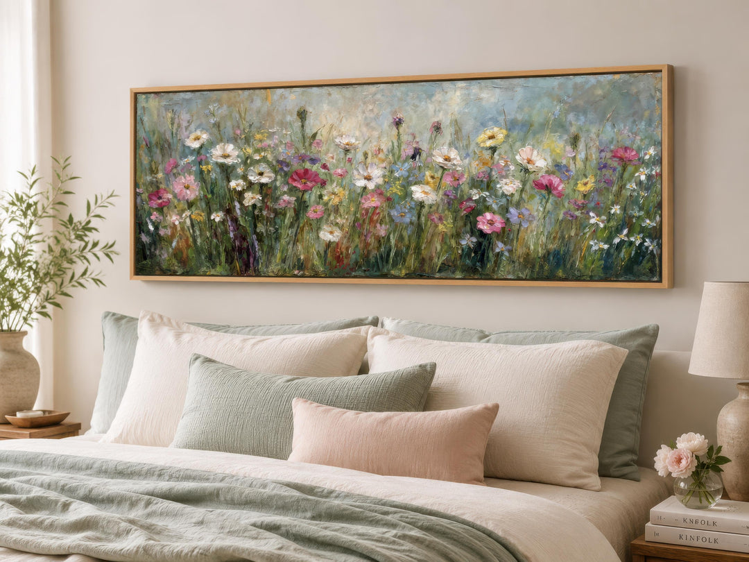 A long narrow canvas painting of a colorful wildflower field hangs above a bed with soft linens.