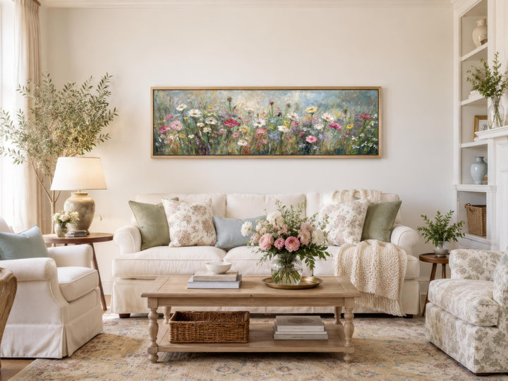 Horizontal wildflower field painting on a long narrow canvas above a white sofa in a living room.