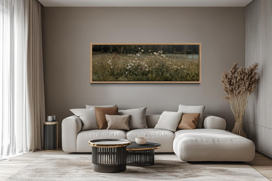 A long, narrow canvas print of a wildflower meadow in a wooden frame above a modern sofa.