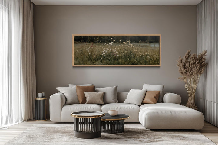 A long, narrow canvas print of a wildflower meadow in a wooden frame above a modern sofa.