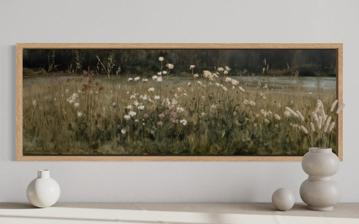 Long narrow canvas print of a wildflower meadow in neutral tones, framed in light wood.