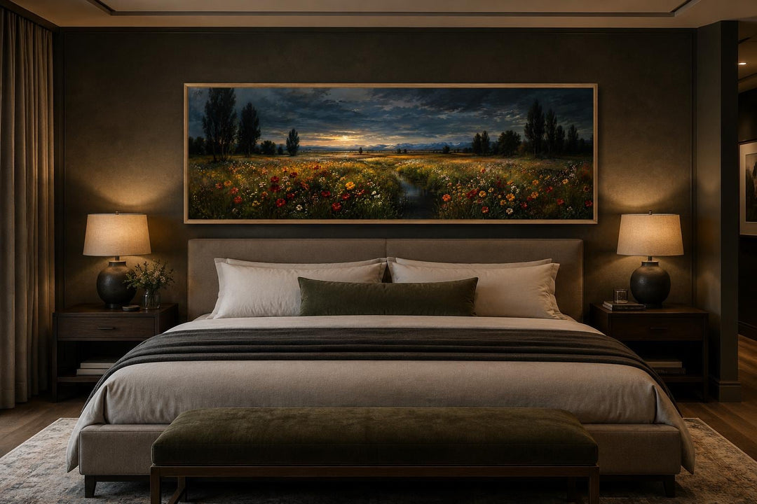 Horizontal canvas wall art of a wildflower meadow at dusk in a slim gold frame above a bed.