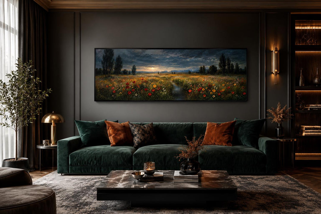 Panoramic wildflower meadow at dusk canvas art above a dark green velvet sofa in a moody room.