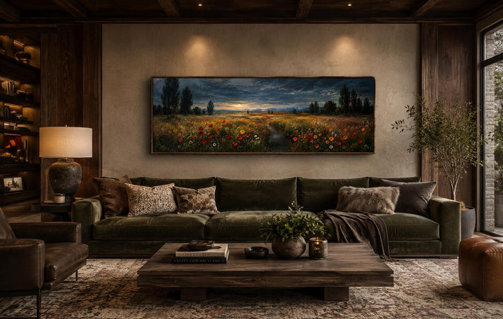 Panoramic wildflower meadow painting at dusk in a gold frame above a green velvet sofa.