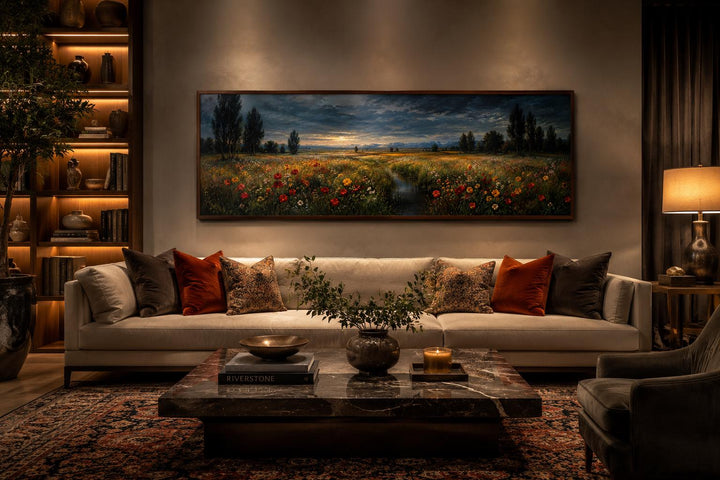 Wide horizontal canvas of a wildflower meadow at dusk with a stream, hung above a modern sofa.
