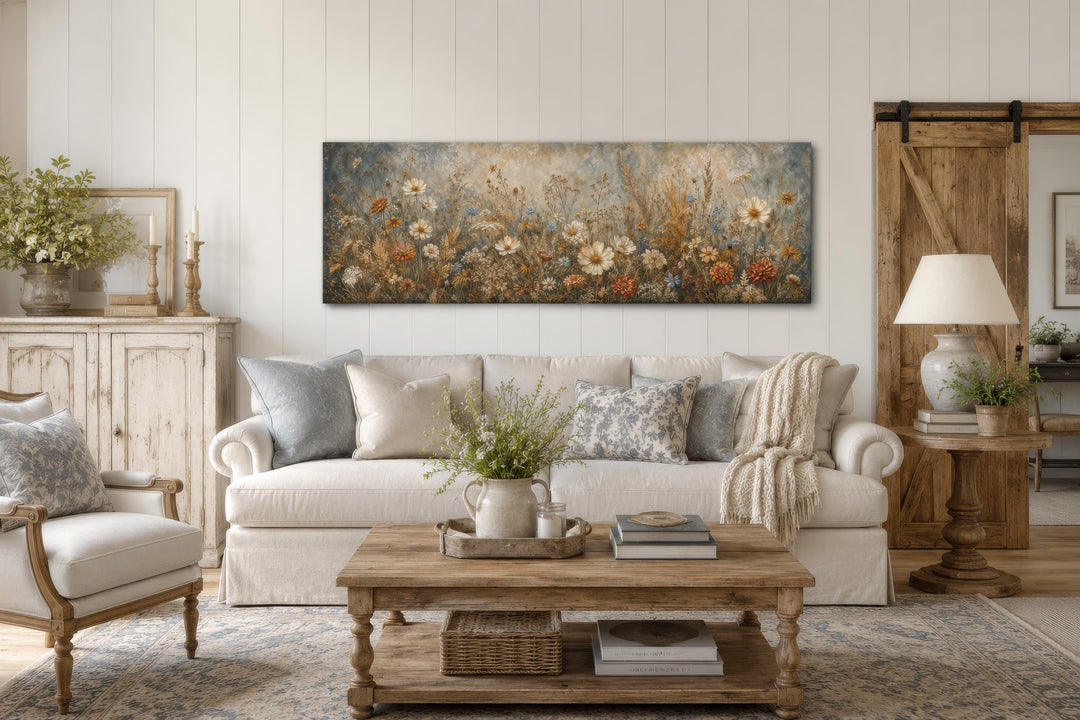 Long narrow canvas print of a neutral wildflower meadow painting above a white sofa.