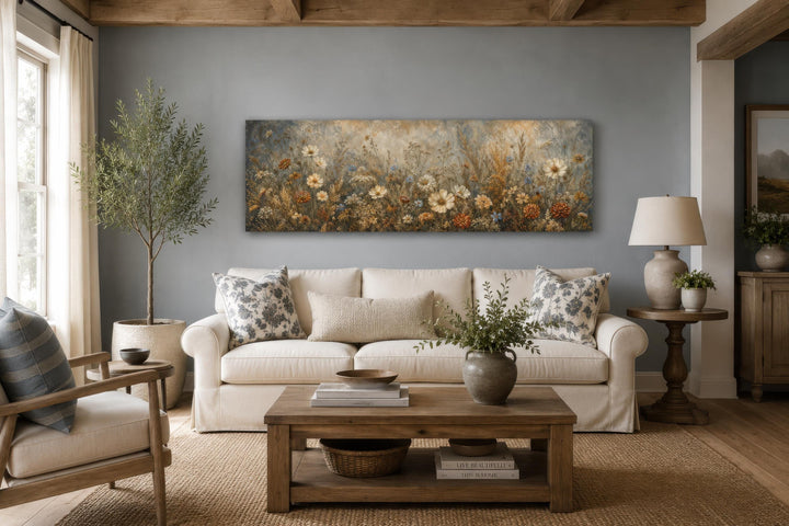 Long narrow canvas print of a neutral wildflower meadow painting above a cream sofa.