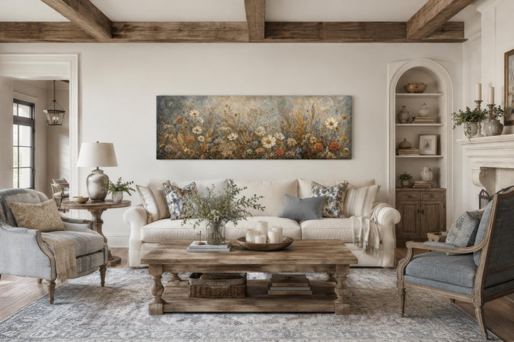 Long narrow horizontal canvas print of a neutral wildflower meadow above a living room sofa.