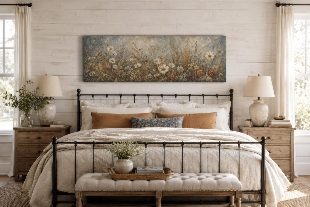 A long narrow canvas print of neutral wildflowers hangs above a bed in a rustic bedroom.