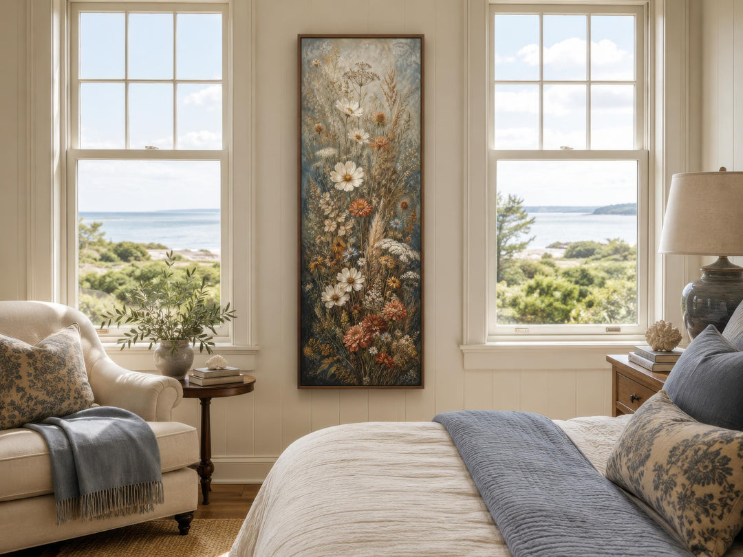 Tall vertical wildflower canvas print in blue, rust, and cream tones hanging in a coastal bedroom.