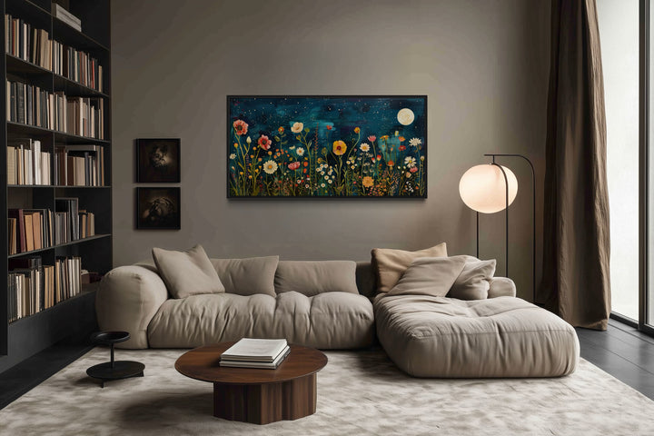 Large horizontal wall art of a wildflower field at night under a full moon above a beige sofa.