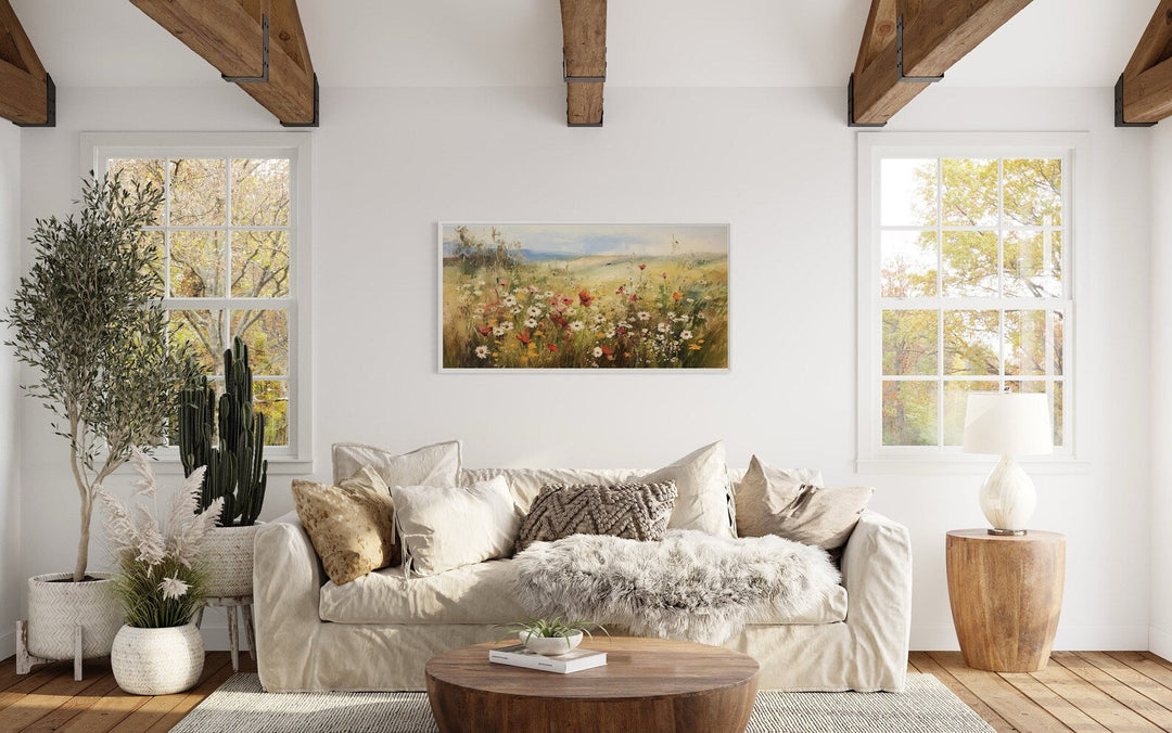 Panoramic farmhouse canvas wall art of a wildflower field above a neutral sofa in a bright room.