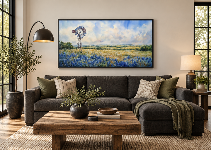 Panoramic canvas wall art of a windmill over a field of bluebonnets above a dark grey sofa.
