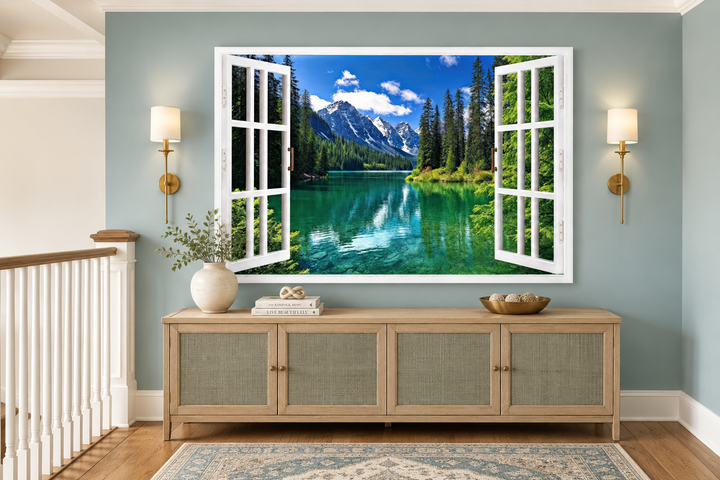 Mountains and emerald lake fake window view wall art in a living room above a wooden sideboard.