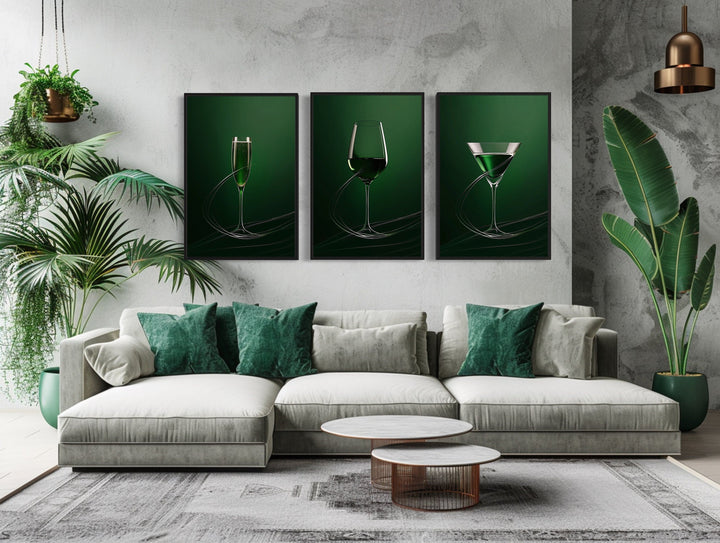 Three-piece framed canvas wall art of emerald green wine, martini, and champagne glasses over a sofa.