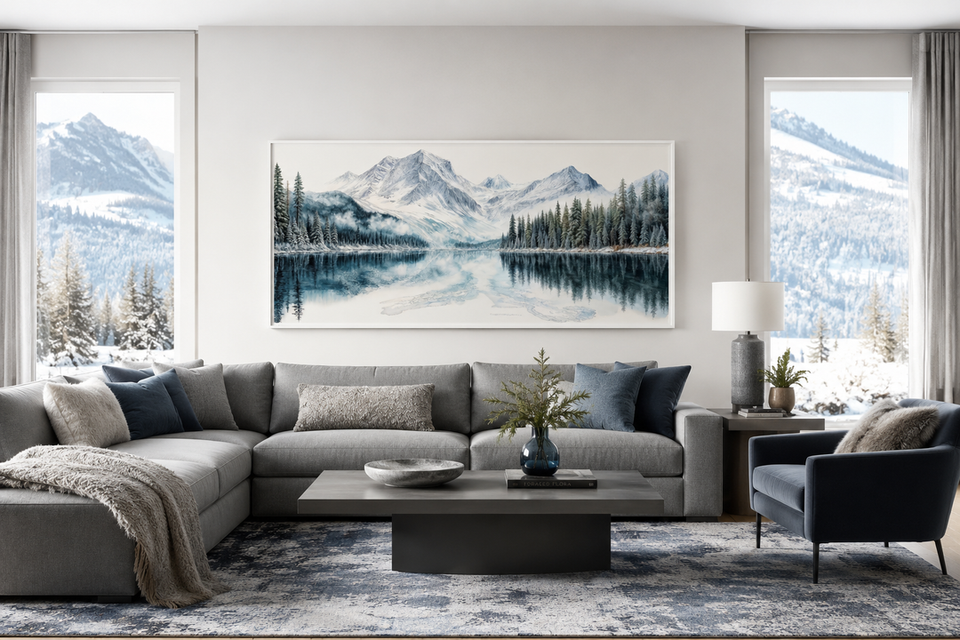 Framed horizontal canvas print of a winter mountain lake and pine forest above a grey sofa.
