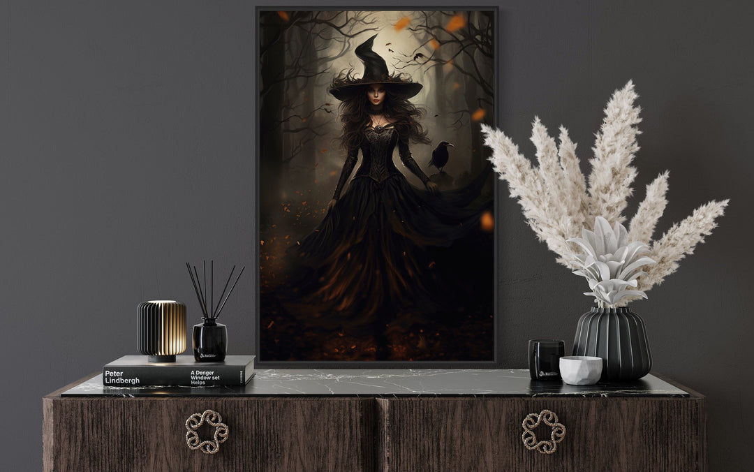 Gothic framed canvas wall art of a witch and her raven in an enchanted forest above a dark sideboard.