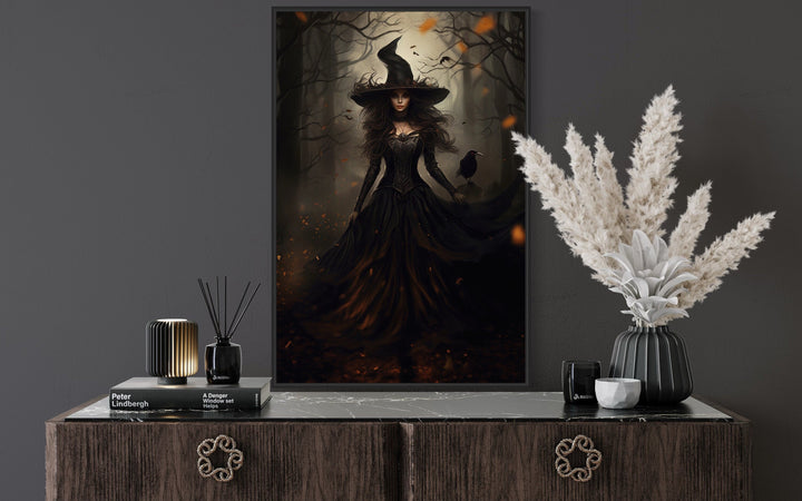 Gothic framed canvas wall art of a witch and her raven in an enchanted forest above a dark sideboard.