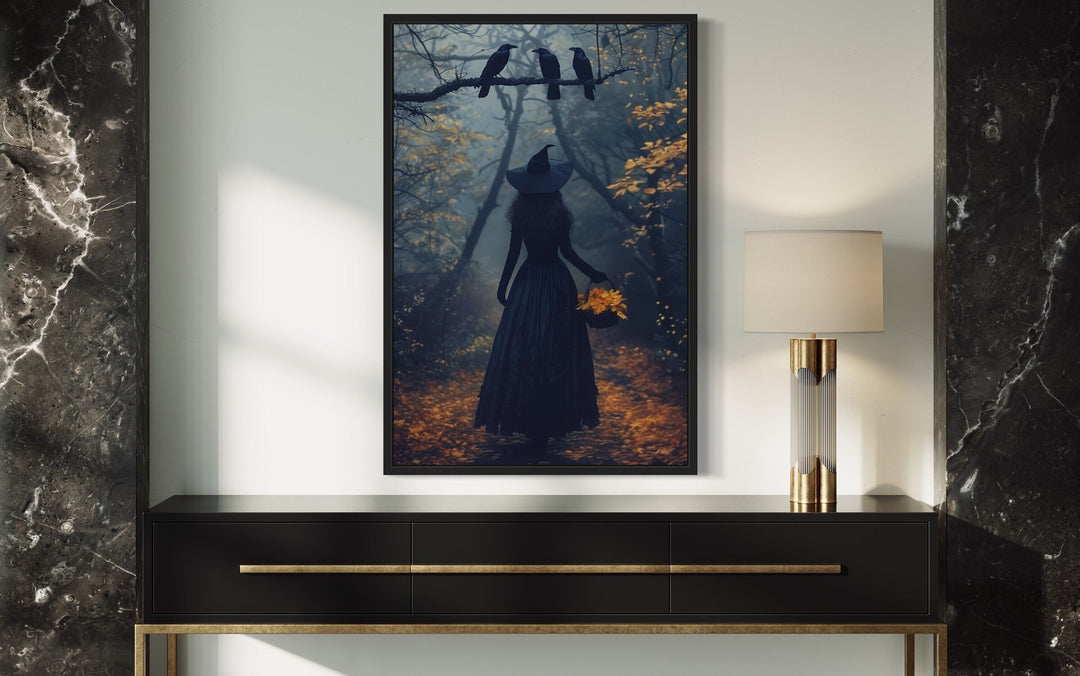 Witch in a misty autumn forest with ravens, framed moody Halloween wall art above a black console.