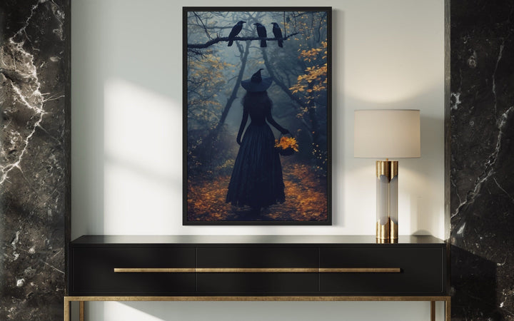Witch in a misty autumn forest with ravens, framed moody Halloween wall art above a black console.